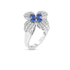 The LOVE IN VERONA DIAMOND AND BLUE SAPPHIRE FLOWER RING by Roberto Coin features a white gold floral design with diamond petals and blue sapphire clusters, elegantly set against a white background.